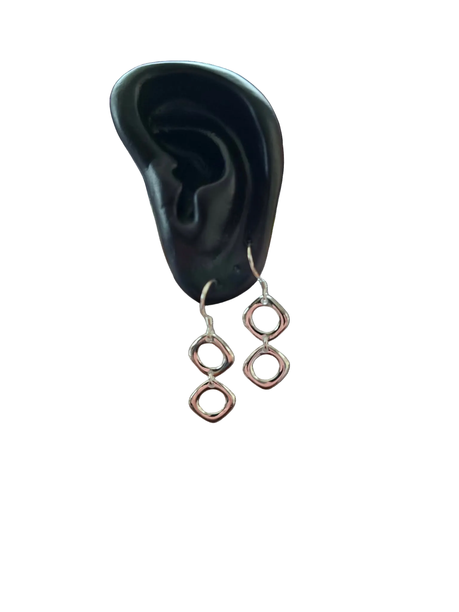Pair of silver earrings displayed in front of a black ear model on a white background